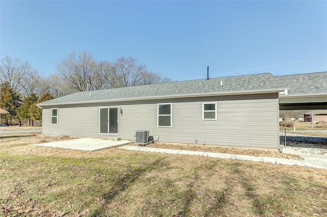 rear view of house featuring roof with shingles, a yard, central AC unit, and a patio