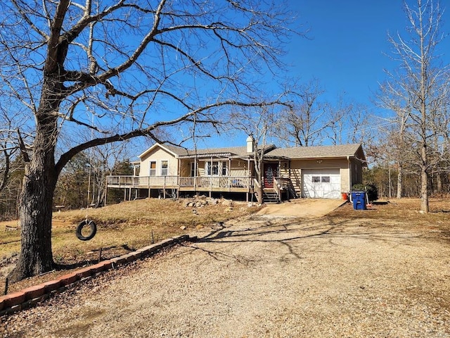 view of front of property with a wooden deck, driveway, a chimney, and an attached garage