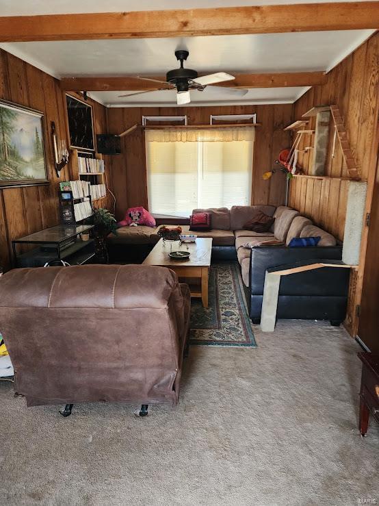 living area with a ceiling fan, carpet, beam ceiling, and wooden walls