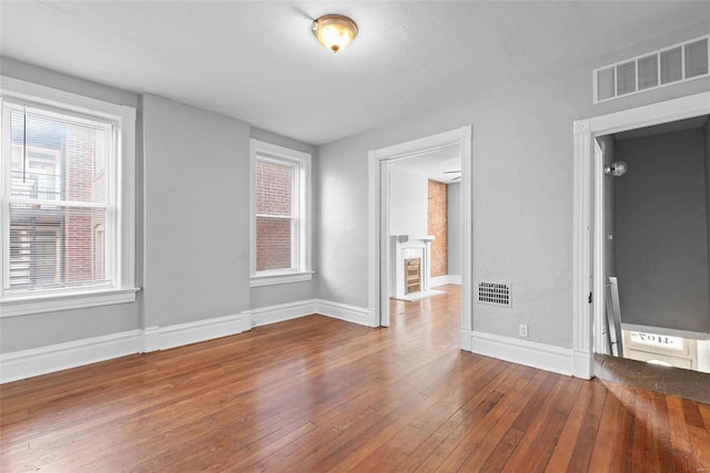 empty room with hardwood / wood-style flooring, plenty of natural light, baseboards, and visible vents