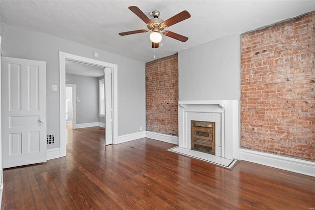 unfurnished living room featuring brick wall, ceiling fan, baseboards, hardwood / wood-style floors, and a fireplace