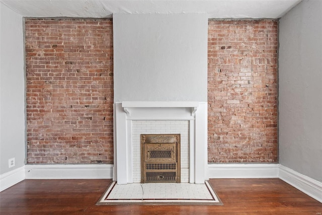 unfurnished living room featuring a fireplace, brick wall, baseboards, and hardwood / wood-style floors