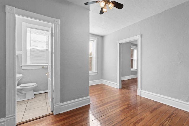 interior space featuring a textured wall, baseboards, wood-type flooring, and ceiling fan