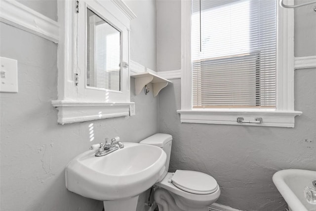 bathroom with a wealth of natural light, toilet, a sink, and a textured wall