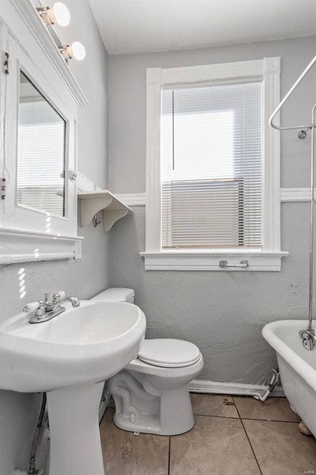 full bathroom featuring a freestanding tub, toilet, a healthy amount of sunlight, and tile patterned flooring