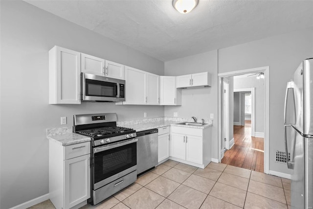 kitchen with light stone counters, a sink, stainless steel appliances, white cabinets, and light tile patterned floors