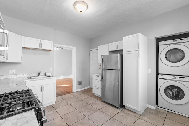 kitchen featuring freestanding refrigerator, a sink, white cabinets, black range with gas stovetop, and stacked washer / dryer