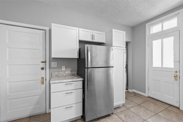 kitchen with white cabinetry, baseboards, freestanding refrigerator, light tile patterned flooring, and a textured ceiling