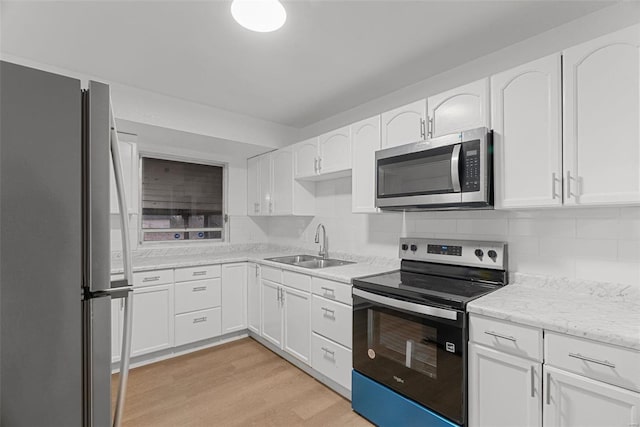 kitchen with a sink, stainless steel appliances, light wood-style floors, and decorative backsplash