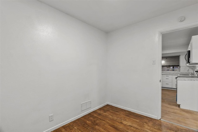 spare room featuring a sink, wood finished floors, visible vents, and baseboards