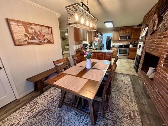 dining area featuring a brick fireplace, baseboards, and light wood finished floors