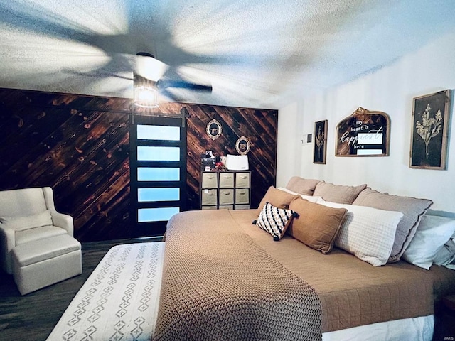 bedroom with wood finished floors, ceiling fan, wood walls, a textured ceiling, and an accent wall