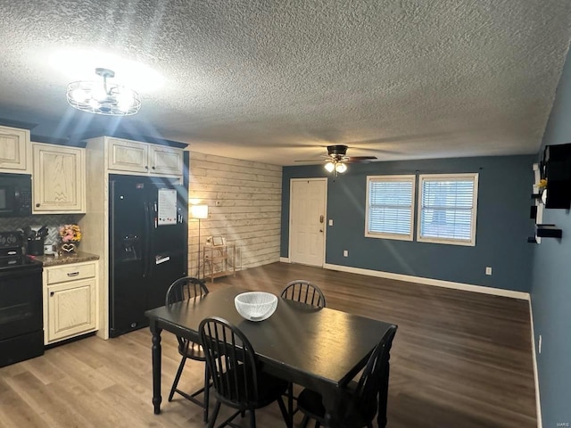 dining room with wooden walls, a textured ceiling, light wood-type flooring, baseboards, and ceiling fan with notable chandelier