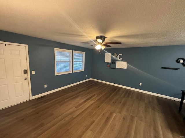 empty room with visible vents, a textured ceiling, baseboards, and dark wood-type flooring