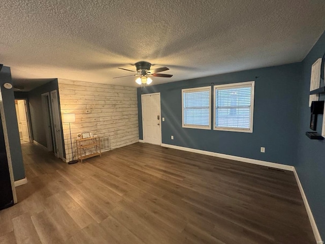 unfurnished living room featuring dark wood-type flooring, wooden walls, baseboards, and a ceiling fan