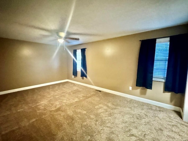 unfurnished room featuring visible vents, baseboards, a ceiling fan, carpet flooring, and a wealth of natural light