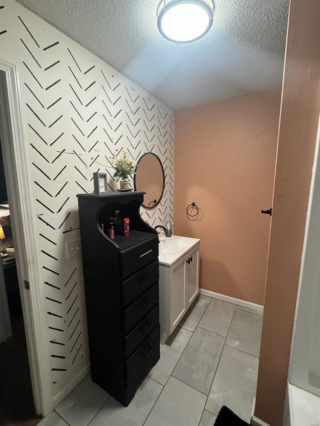 bathroom with baseboards, an accent wall, tile patterned floors, a textured ceiling, and vanity