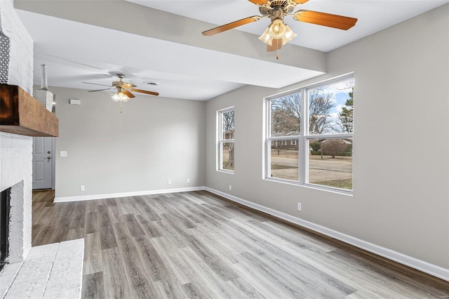 unfurnished living room featuring a brick fireplace, ceiling fan, baseboards, and wood finished floors