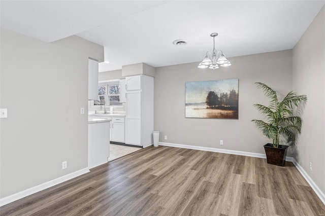 unfurnished dining area featuring a notable chandelier, wood finished floors, visible vents, and baseboards