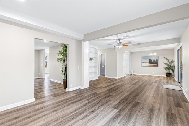 unfurnished living room featuring ceiling fan with notable chandelier, wood finished floors, and baseboards