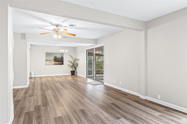 unfurnished living room with ceiling fan with notable chandelier, wood finished floors, visible vents, and baseboards