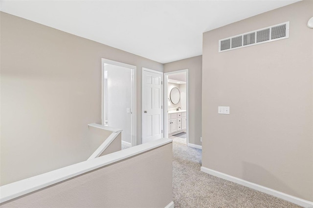 hall with light carpet, baseboards, and visible vents