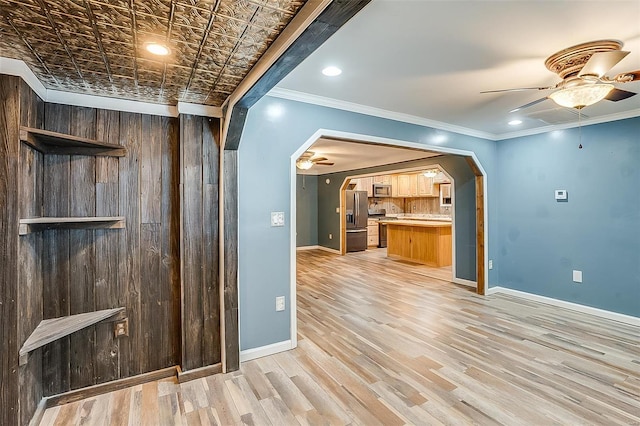 spare room with baseboards, light wood finished floors, arched walkways, ceiling fan, and crown molding