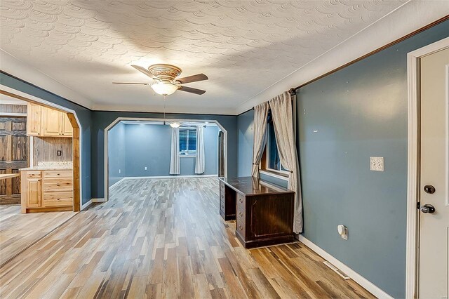 interior space featuring arched walkways, light brown cabinets, a textured ceiling, and light wood-style floors