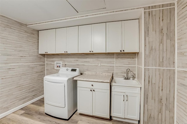 laundry room featuring wooden walls, light wood finished floors, washer / dryer, cabinet space, and a sink