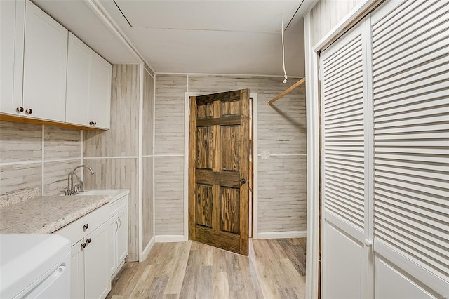 laundry room with cabinet space, light wood-style floors, wood walls, and a sink