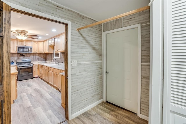 kitchen with wooden walls, light brown cabinets, light countertops, light wood-style floors, and stainless steel appliances