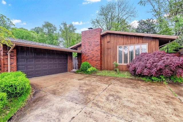 view of side of property featuring a garage, board and batten siding, driveway, and a chimney