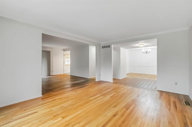 unfurnished living room with an inviting chandelier, visible vents, and hardwood / wood-style flooring