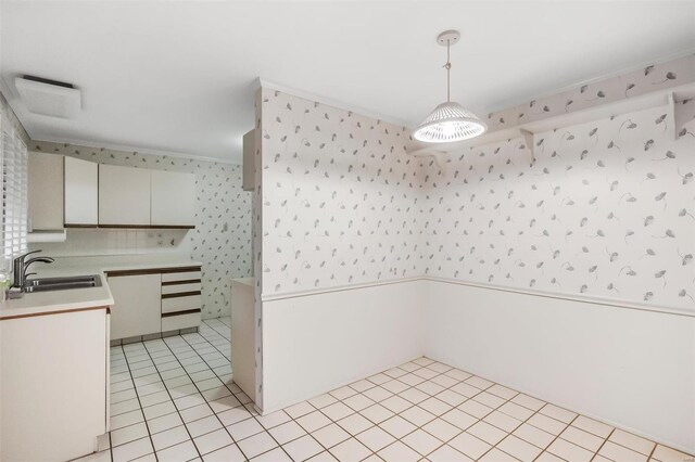 kitchen with hanging light fixtures, a sink, light countertops, wallpapered walls, and light tile patterned flooring