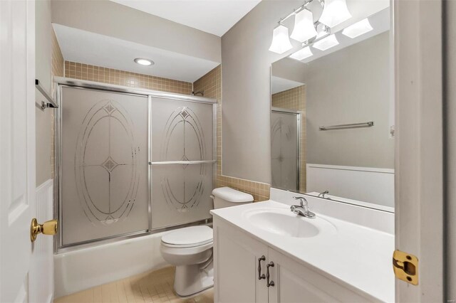 full bathroom featuring vanity, toilet, shower / bath combination with glass door, and tile walls