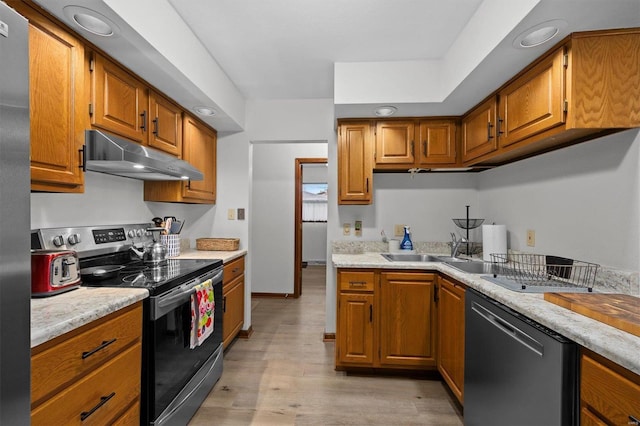 kitchen with under cabinet range hood, light wood-style floors, light countertops, appliances with stainless steel finishes, and brown cabinetry