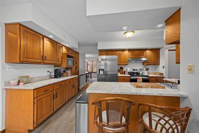 kitchen with light wood-style flooring, under cabinet range hood, stainless steel appliances, a peninsula, and a kitchen bar