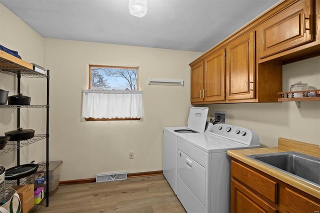 washroom featuring separate washer and dryer, a sink, visible vents, light wood-style floors, and cabinet space