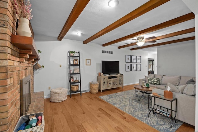 living room featuring wood finished floors, visible vents, baseboards, a brick fireplace, and beam ceiling