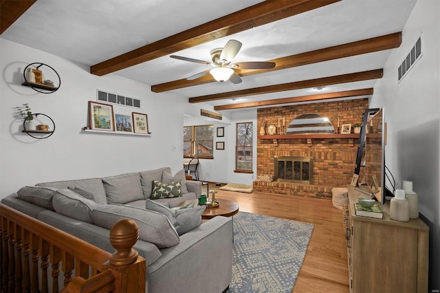 living room featuring light wood-style floors, a brick fireplace, visible vents, and ceiling fan