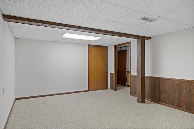 finished basement with wooden walls, visible vents, a paneled ceiling, wainscoting, and carpet floors