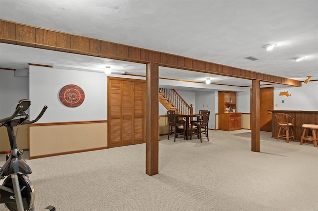 finished basement with wood walls, visible vents, stairway, a dry bar, and carpet