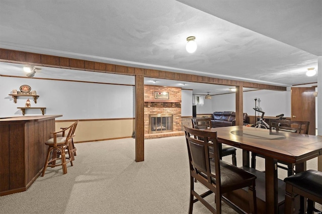 dining space featuring wooden walls, a brick fireplace, light carpet, and indoor bar