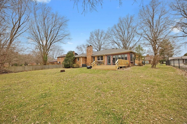 rear view of house with fence, a chimney, a wooden deck, and a lawn