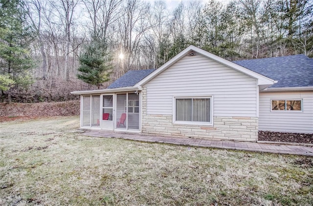 back of property featuring stone siding, a lawn, a sunroom, and a shingled roof