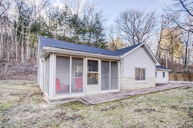 back of house with fence, roof with shingles, a lawn, a sunroom, and stone siding