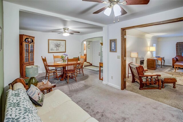 carpeted living room featuring baseboards, arched walkways, and ceiling fan