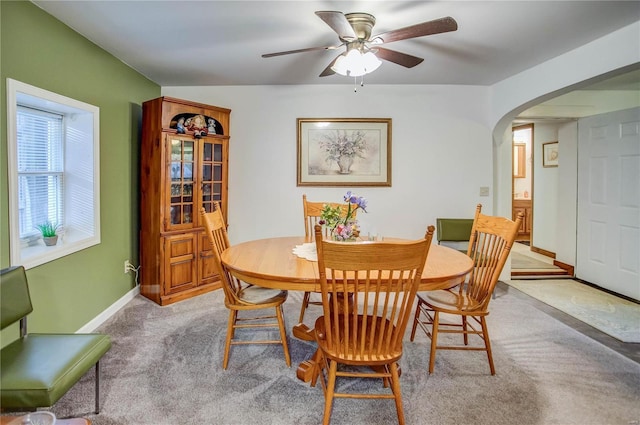 dining area with a ceiling fan, baseboards, arched walkways, and light carpet