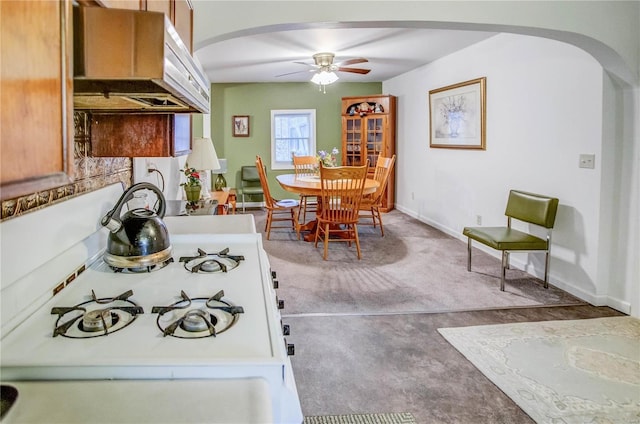 kitchen featuring white gas stove, range hood, arched walkways, baseboards, and ceiling fan