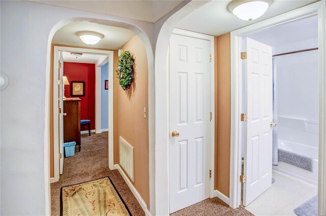 corridor featuring arched walkways, visible vents, light carpet, and baseboards